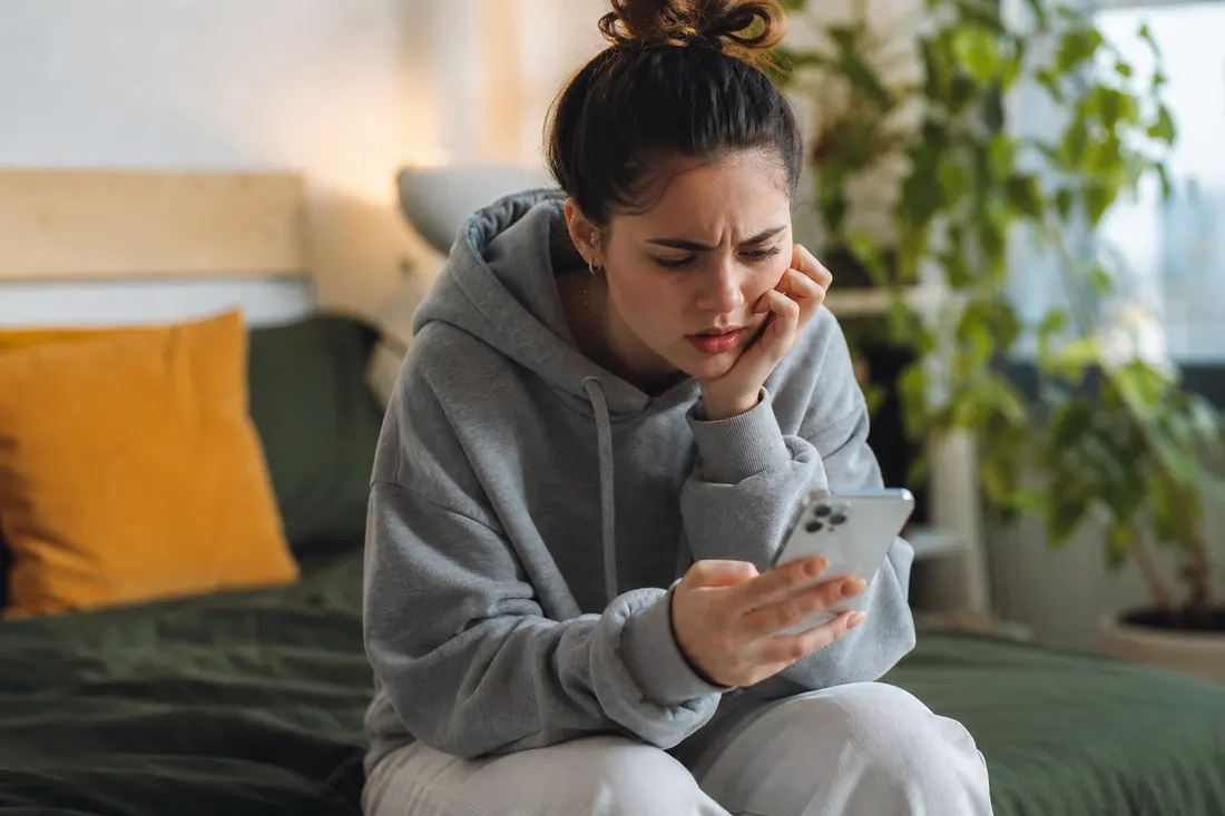 Jeune assis chez lui, regardant son téléphone d'un air perplexe en consultant les statistiques d'un post