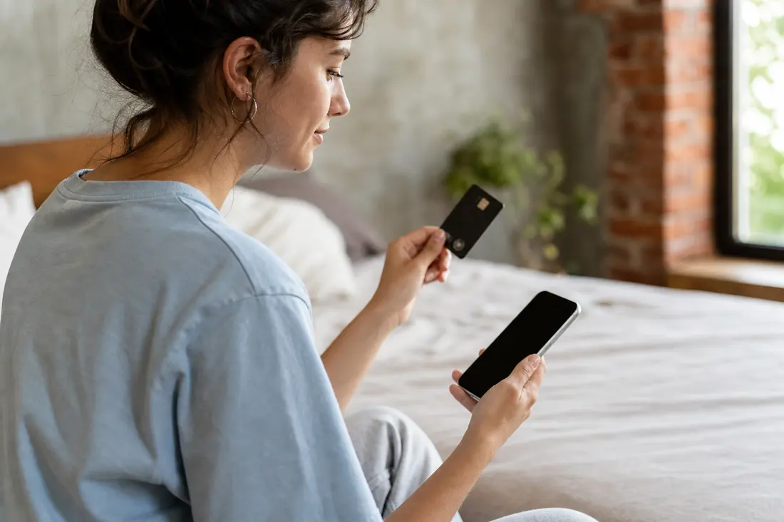 Jeune personne qui paie en ligne avec sa carte bancaire et son téléphone à la main
