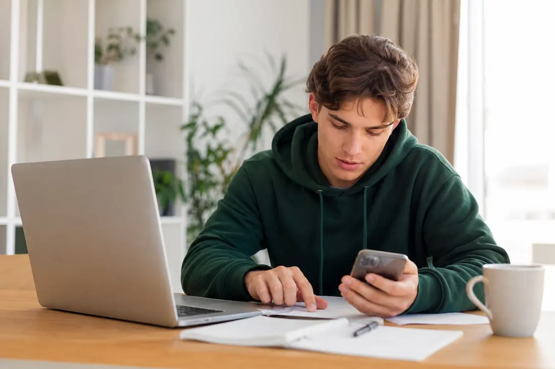 Jeune personne assise avec son ordinateur portable et son téléphone, gérant ses abonnements en ligne