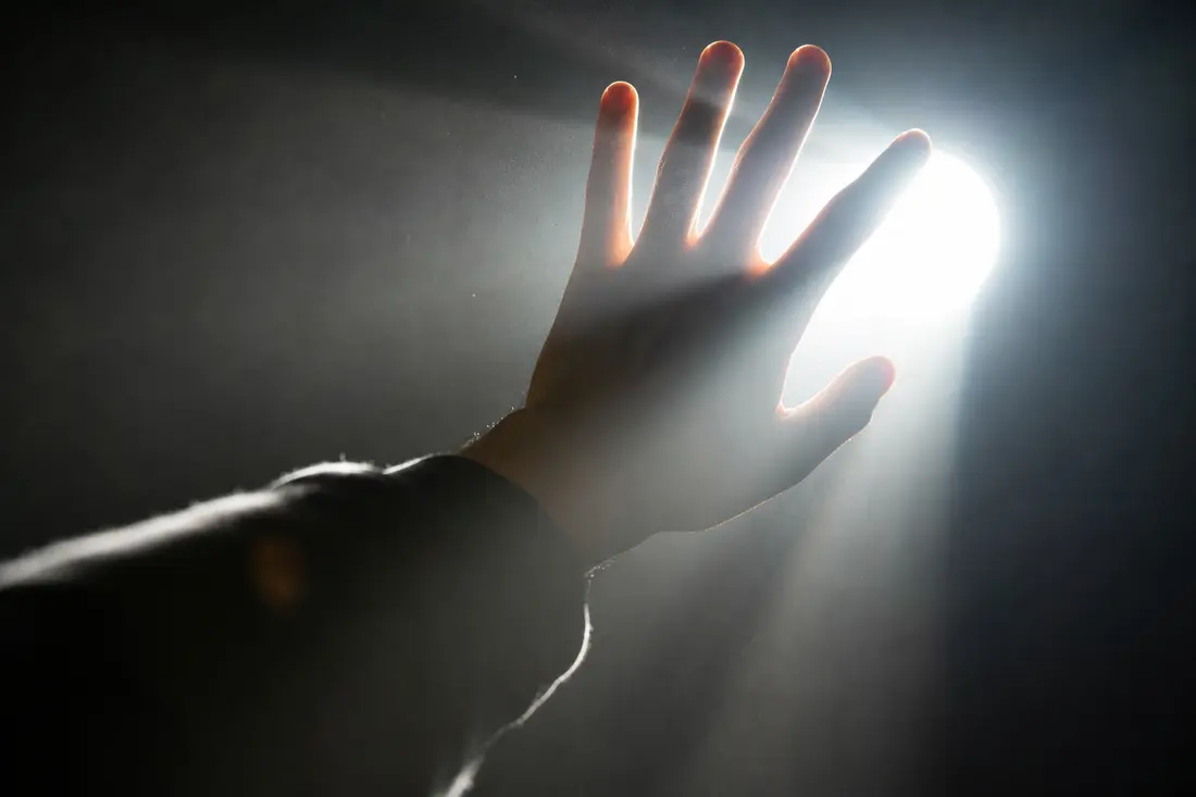 Main tentant de bloquer une lumière vive, la clarté filtrant entre les doigts, sur fond de ville animée le soir