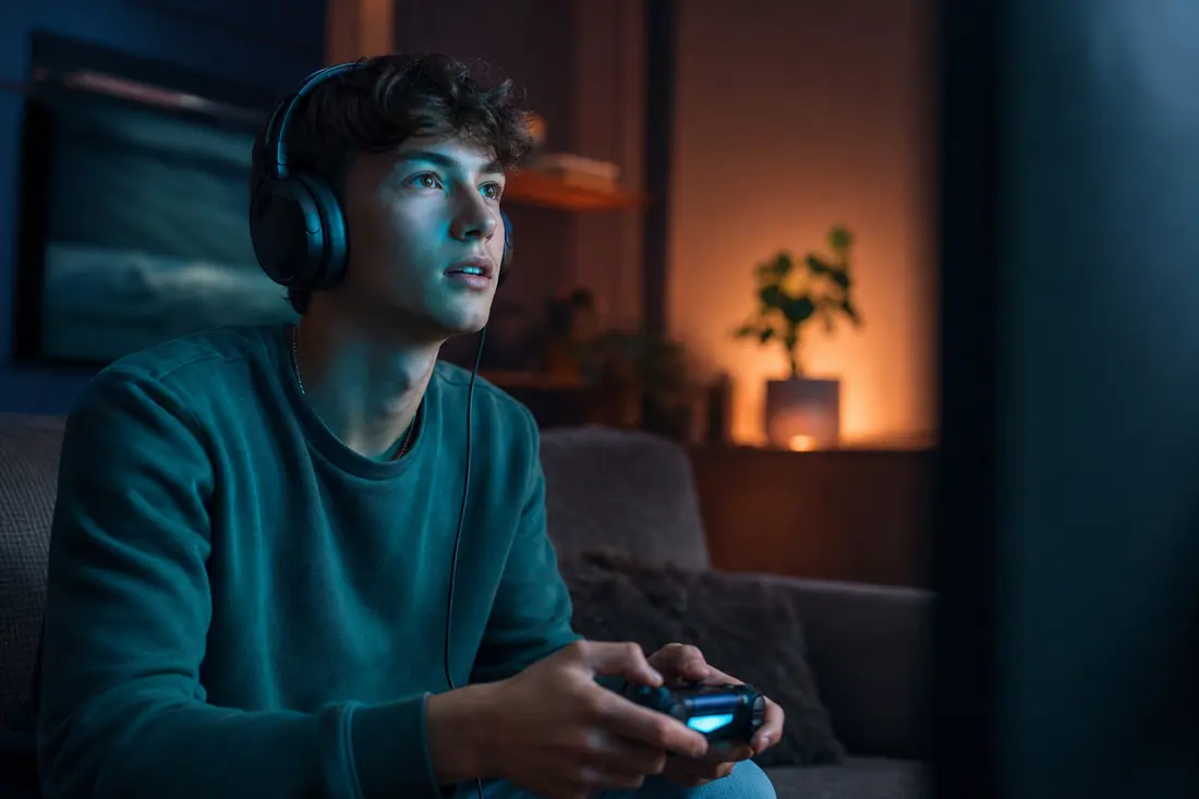 Jeune joueur devant son écran avec une manette, interface de jeu vidéo colorée en arrière-plan
