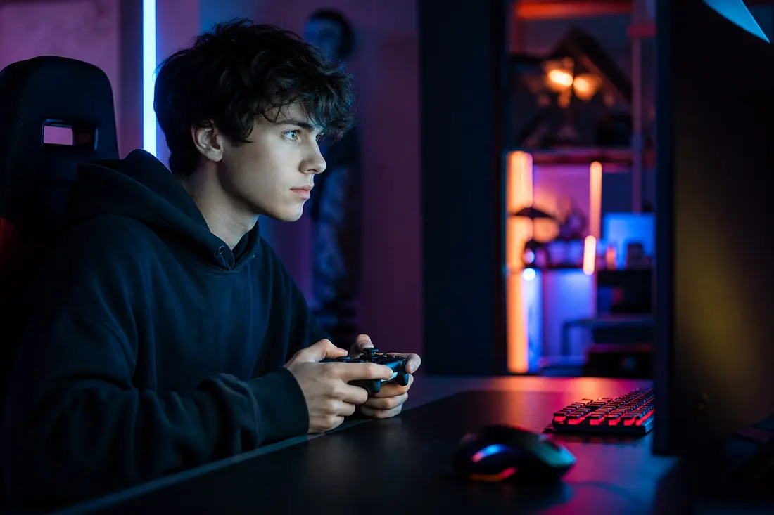 Joueur concentré manette en main devant un écran de jeu vidéo, ambiance gaming aux lumières colorées