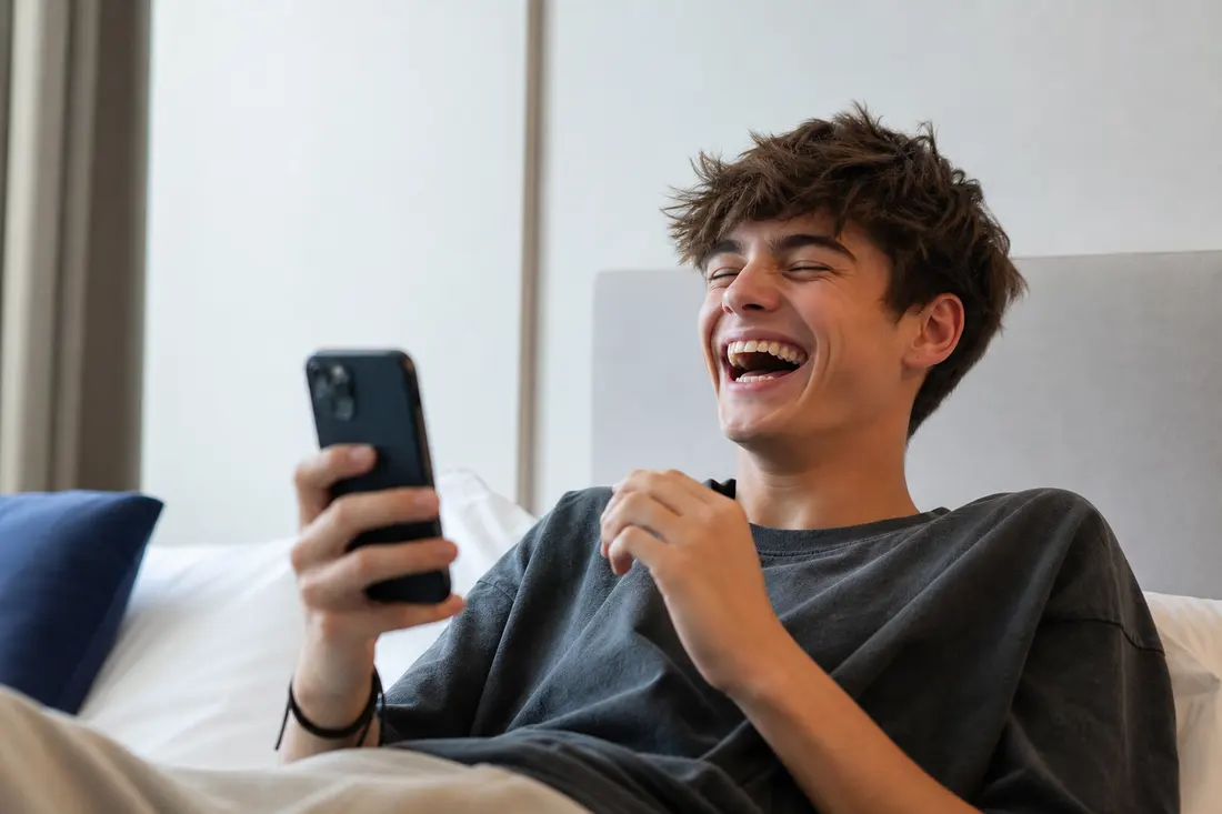 Jeune personne riant aux éclats devant son téléphone, expression spontanée et joyeuse