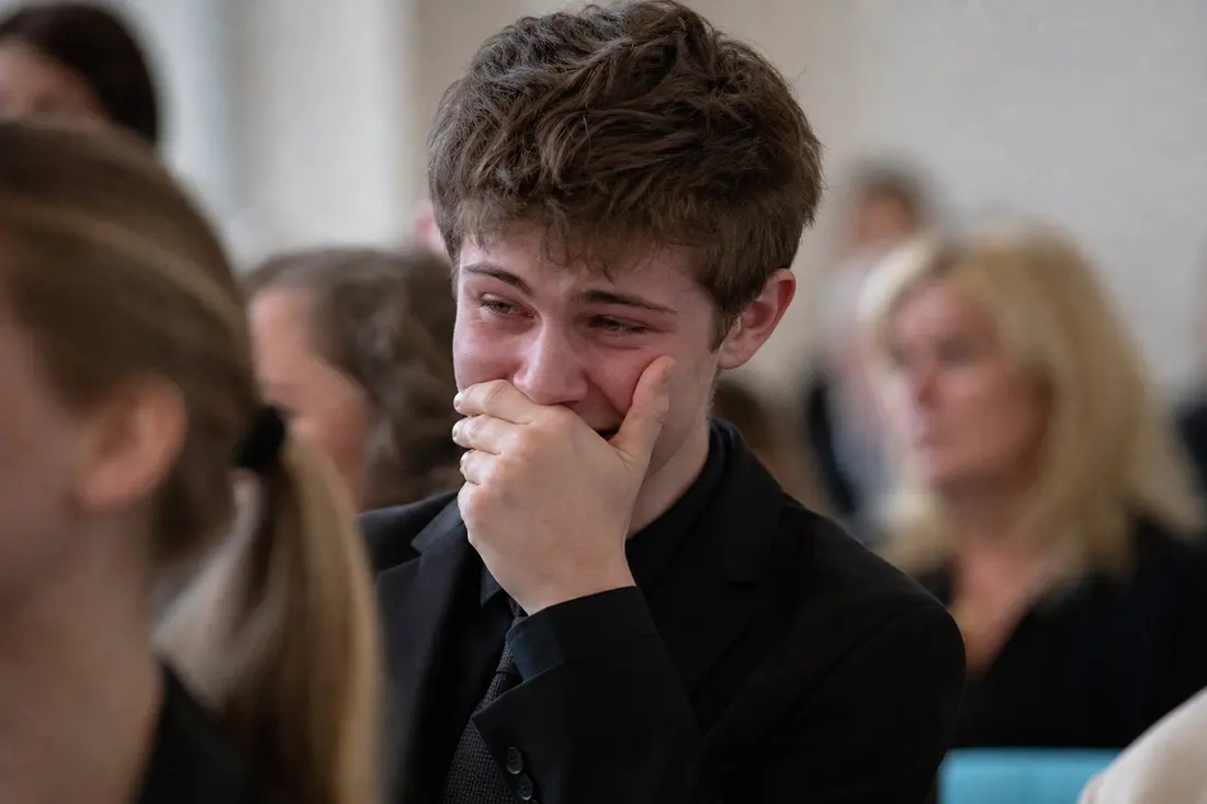 Jeune assis en rang, la main plaquée sur la bouche, essayant visiblement de retenir un fou rire