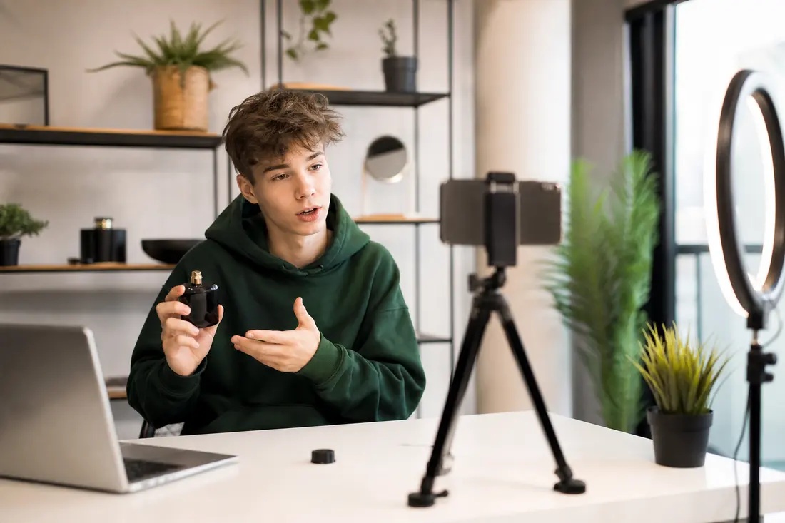 Jeune créatrice de contenu filmant une vidéo avec son smartphone, entourée de produits posés sur un bureau