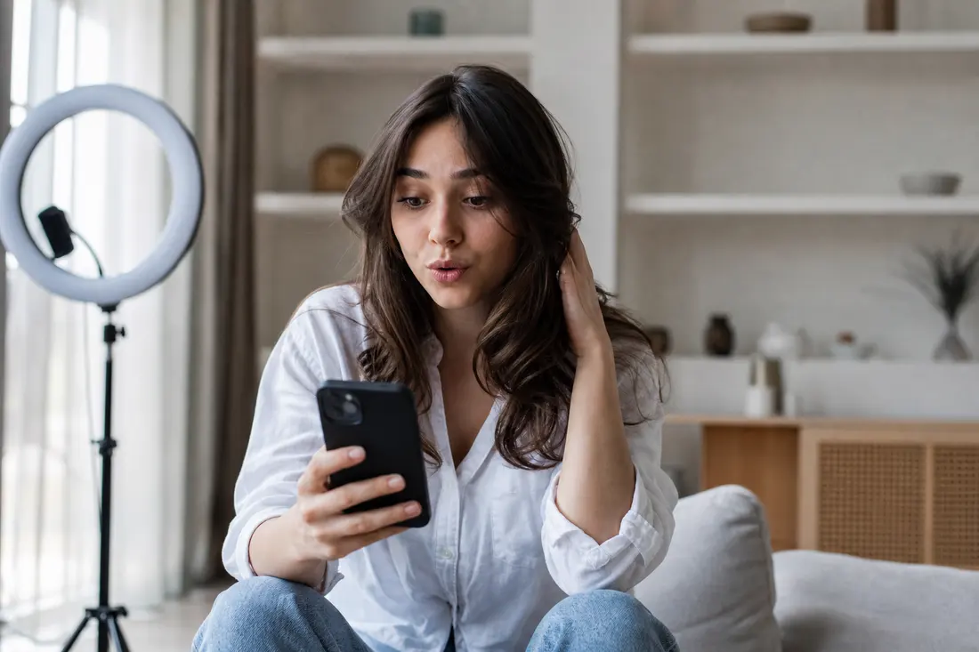 Jeune femme souriante consultant son téléphone avec l'interface d'un réseau social, ambiance lumineuse et moderne