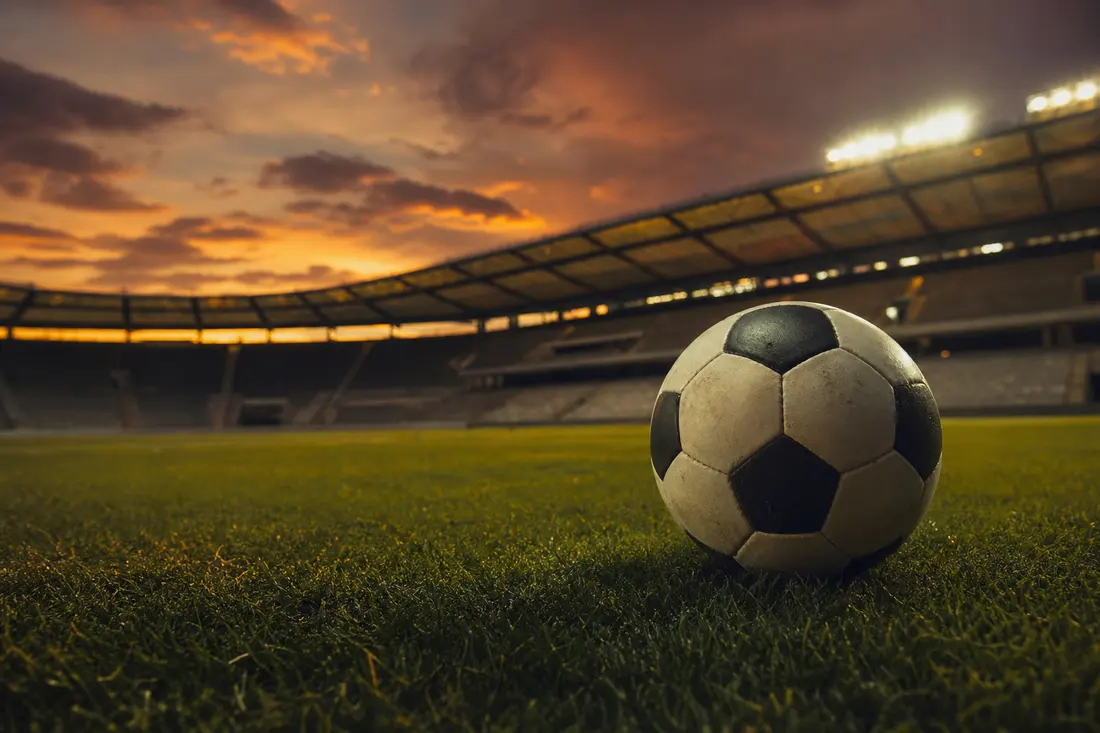Ballon de football posé sur une pelouse au stade, ambiance dramatique en fin de journée