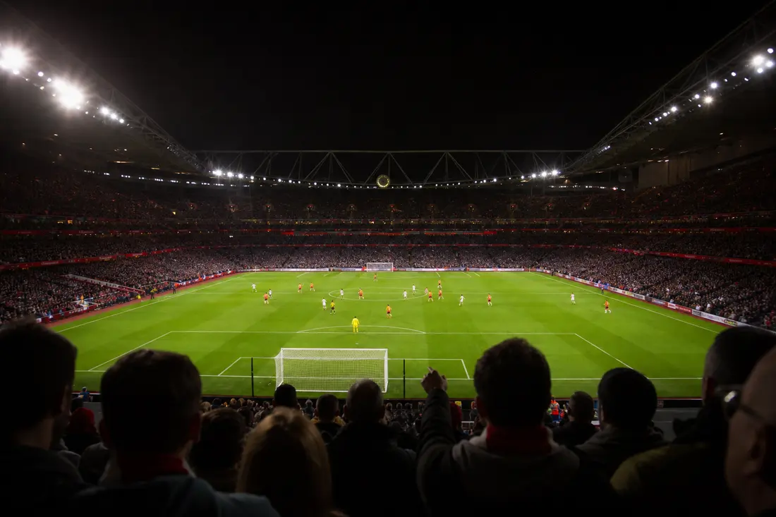 Stade de football vu de nuit avec l'horloge du match et les projecteurs allumés