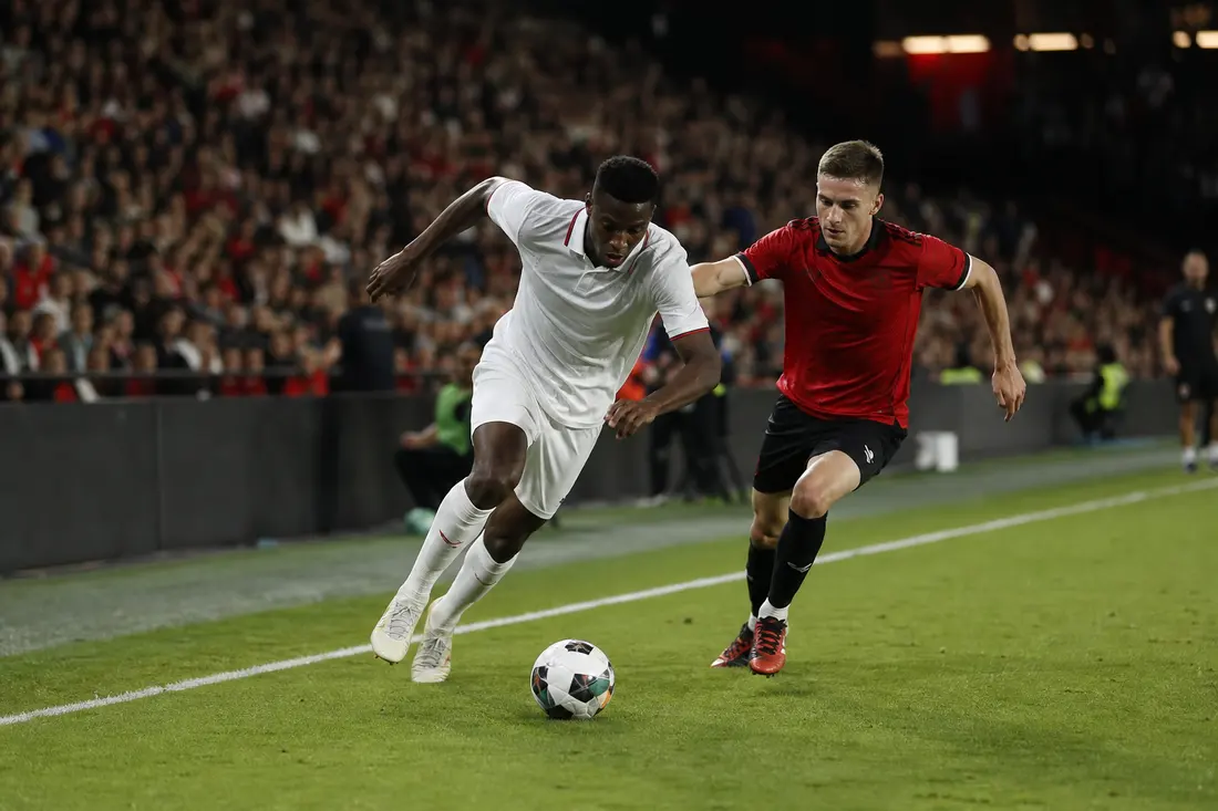 Joueurs de football alignés sur le terrain au moment d'une passe décisive, sous les projecteurs du stade