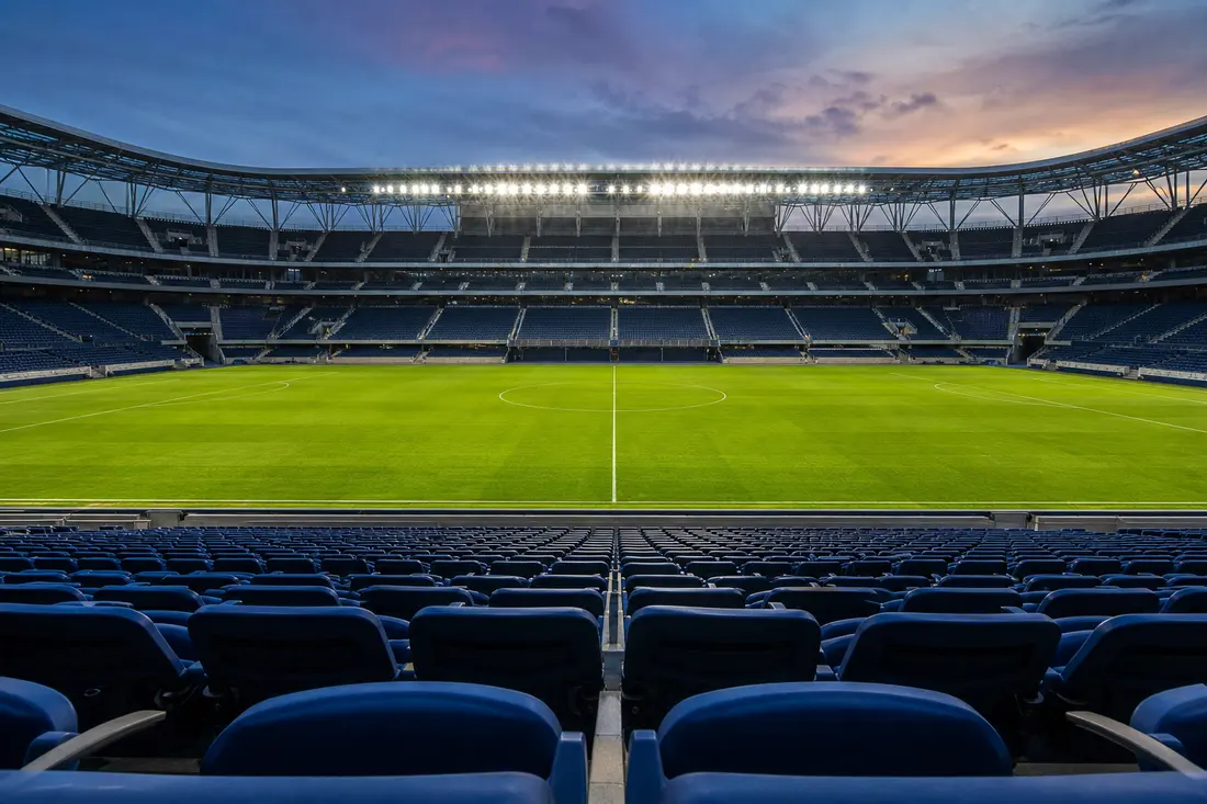 Stade de football vide avec pelouse éclairée et tribunes totalement désertes en fin de journée