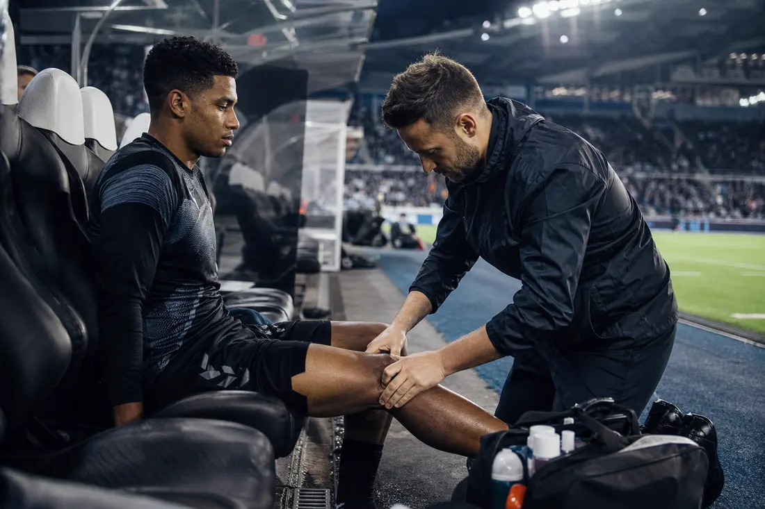 Joueur de football au sol sur la pelouse d'un stade, staff médical penché au-dessus de lui