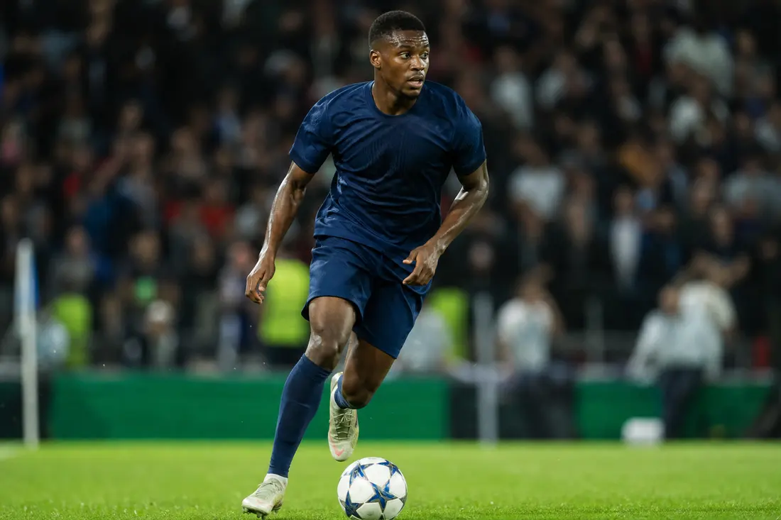Joueur de football en action sur la pelouse d'un stade, ballon au pied, sous les projecteurs
