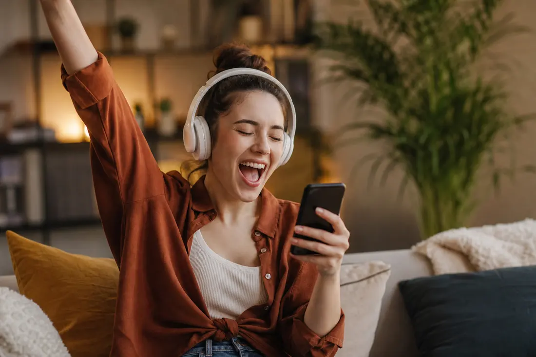 Jeune personne surprise et enthousiaste en écoutant de la musique avec des écouteurs, téléphone à la main