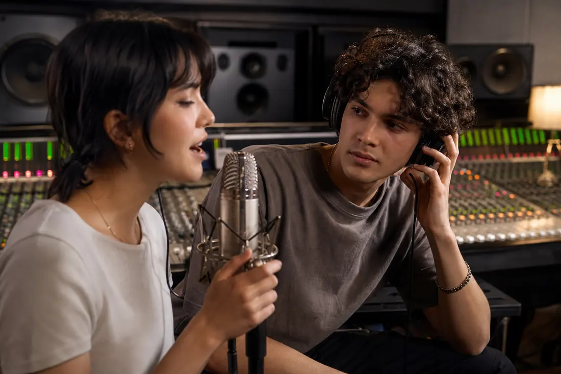 Deux artistes en studio d'enregistrement, casques audio sur les oreilles, en train de collaborer devant un micro