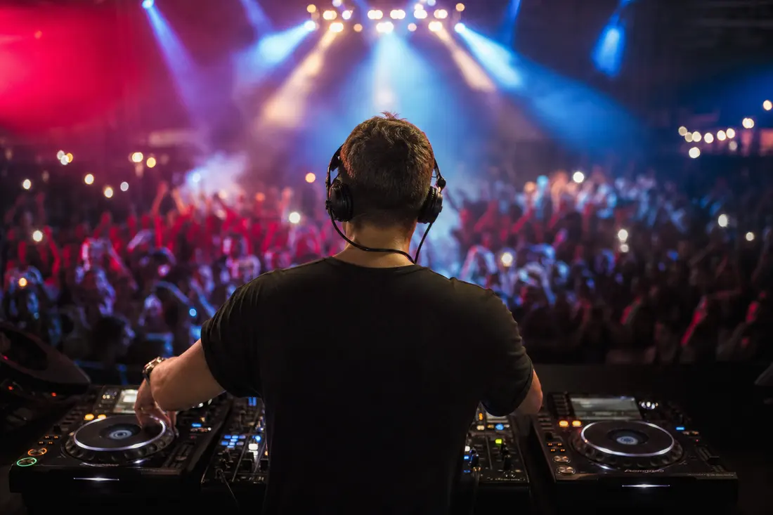 DJ mixant deux morceaux sur des platines dans une ambiance de concert aux lumières colorées